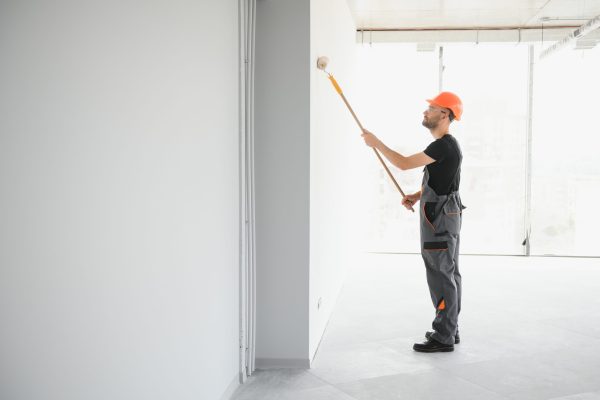 Portrait of man holding paint roller while painting white wall and making renovation.