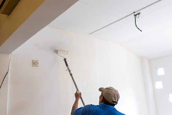 Worker painting wall with new coat of paint using paint roller during renovation project